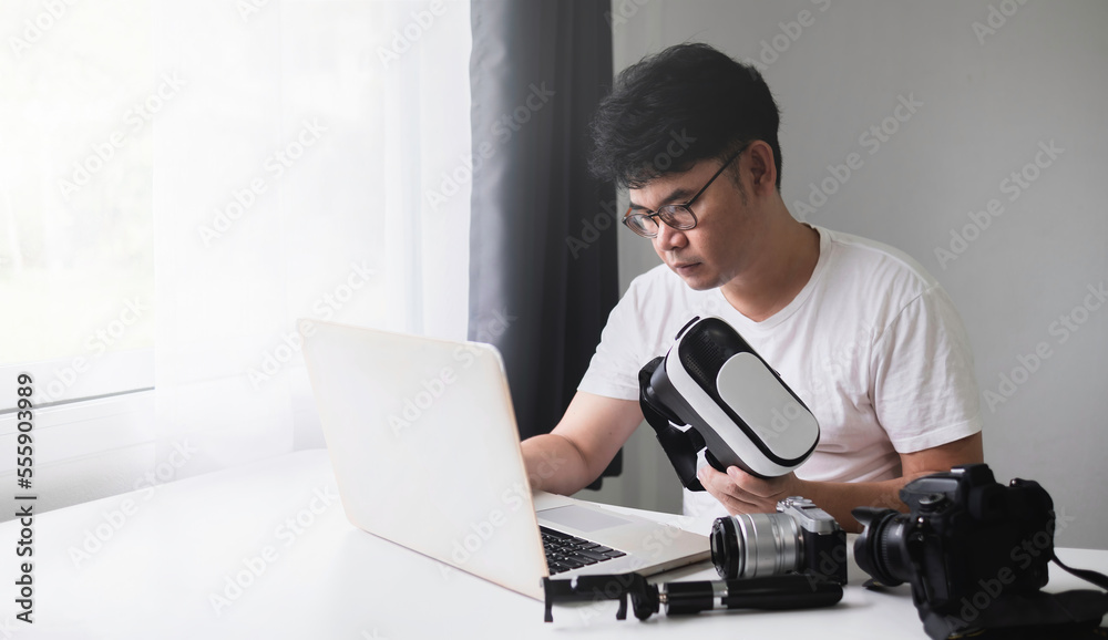 Content Creator for Virtual Reality and Metaverse Concept, Asian man using laptop to edit video, from camera, for VR glasses. Content Creator for Virtual Reality and Metaverse Concept, Asian man using laptop to edit video, from camera, for VR glasses.