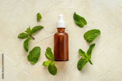 Bottle of essential peppermint oil with fresh green mint leaves