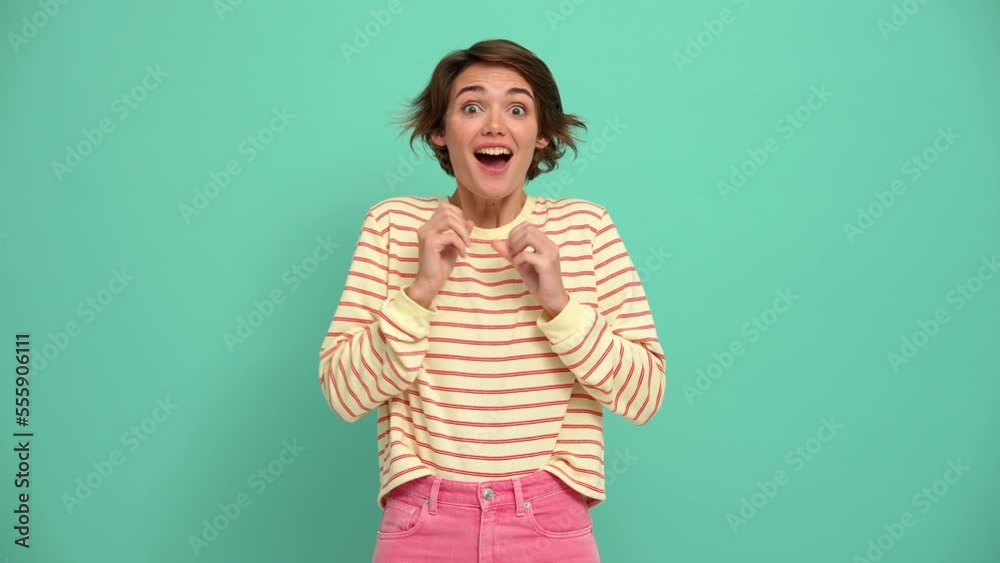 Worried young woman with short hairstyle rejoicing at the camera in the turquoise studio Worried young woman with short hairstyle rejoicing at the camera in the turquoise studio