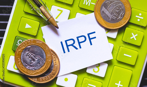 As iniciais IRPF escritas em cor azul em um pequeno pedaço de papel. Caneta e Calculadora na composição. Economia brasileira, imposto de renda. photo