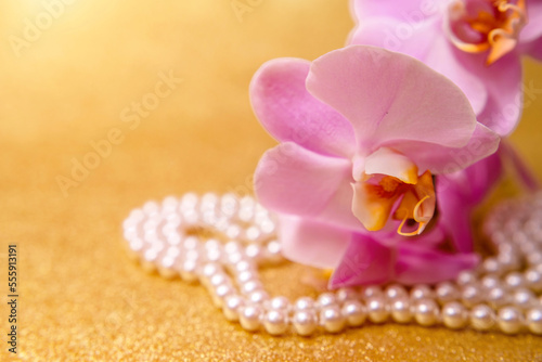 purple Orchid and pearl necklace on a shiny gold background
