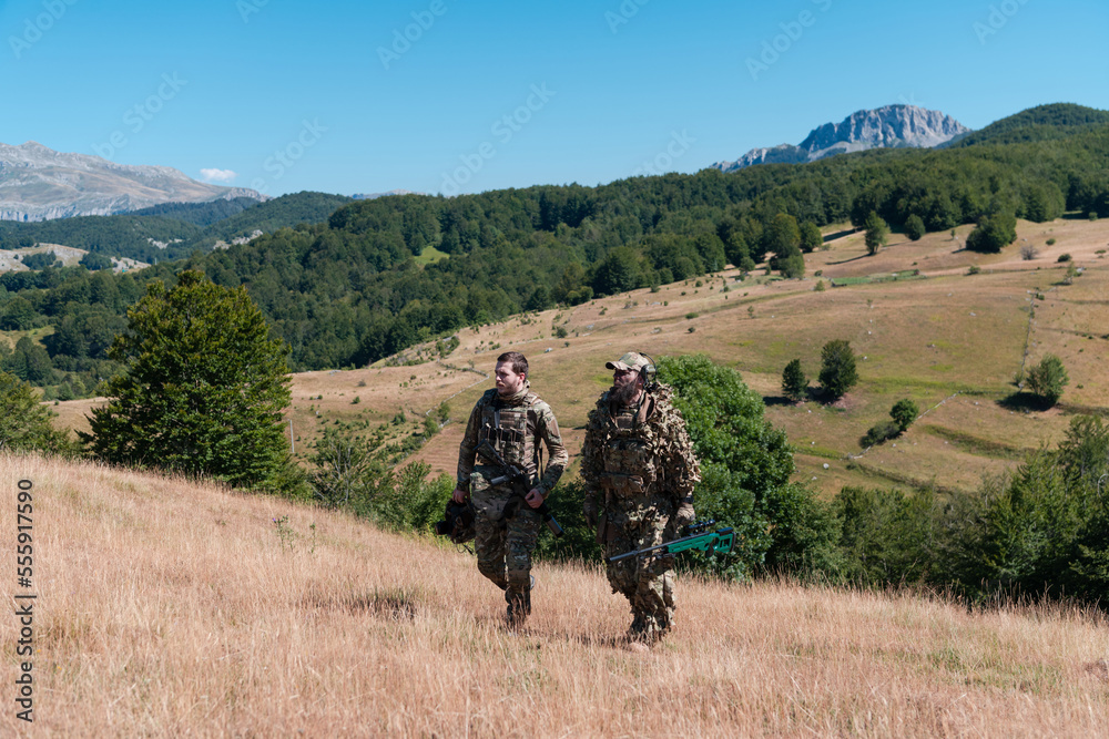A sniper team squad of soldiers is going undercover. Sniper assistant and team leader walking and aiming in nature with yellow grass and blue sky. Tactical camouflage uniform. A sniper team squad of soldiers is going undercover. Sniper assistant and team leader walking and aiming in nature with yellow grass and blue sky. Tactical camouflage uniform.
