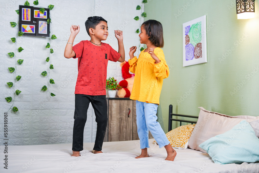 Happy smiling sibling kids dancing by jumping on bed at home - concept of playful childhood, bonding and relationship. Happy smiling sibling kids dancing by jumping on bed at home - concept of playful childhood, bonding and relationship.