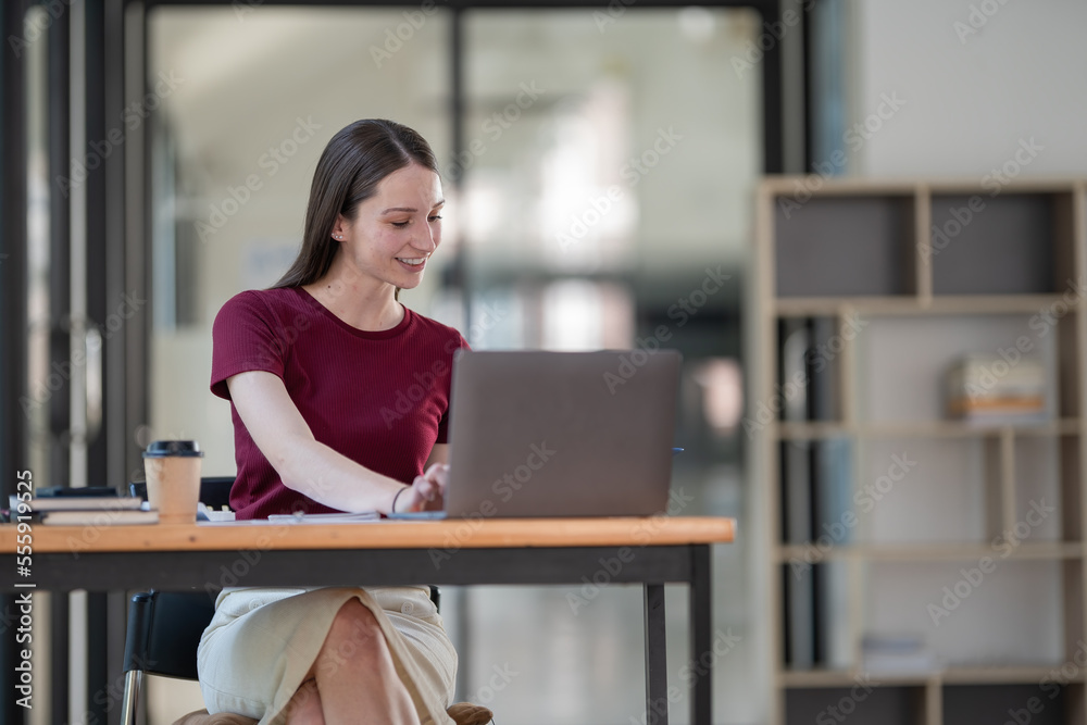 Concentrated at work. Confident young woman in smart casual wear working on a laptop while sitting near a window in a creative office or cafe.