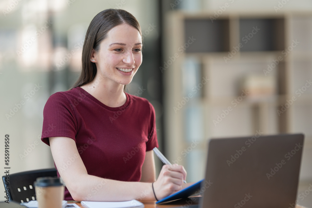 Concentrated at work. Confident young woman in smart casual wear working on a laptop while sitting near a window in a creative office or cafe. Concentrated at work. Confident young woman in smart casual wear working on a laptop while sitting near a window in a creative office or cafe.