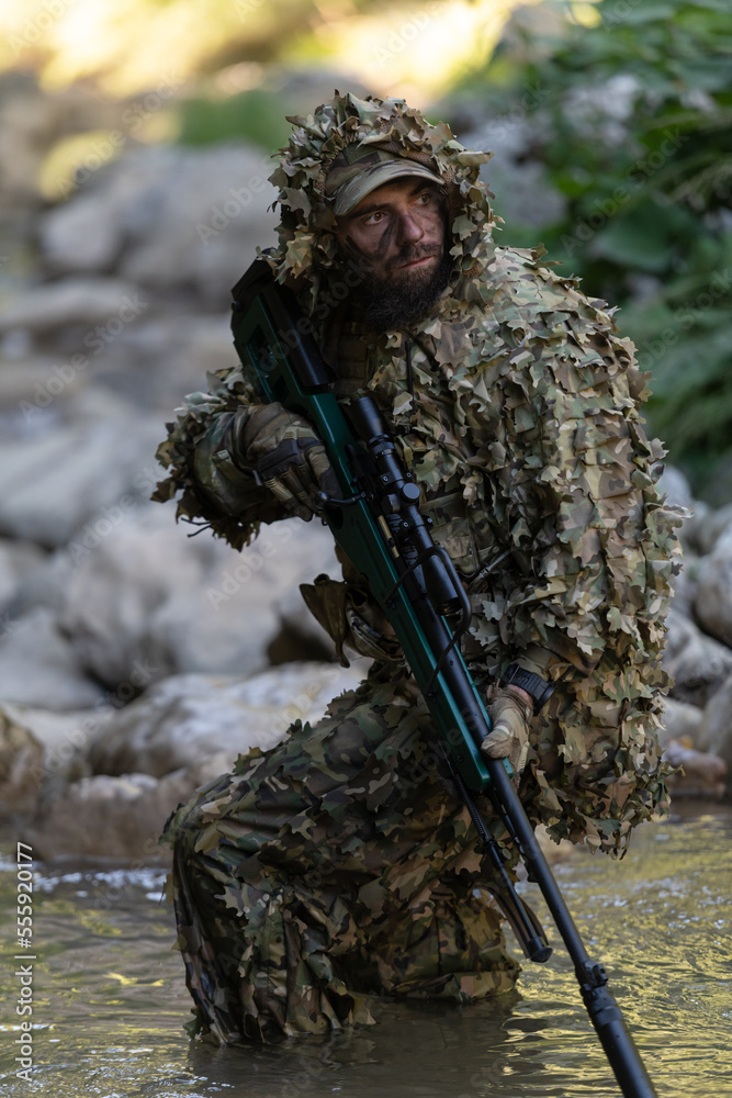 A military man or airsoft player in a camouflage suit sneaking the river  and aims from a sniper rifle to the side or to target. Stock Photo | Adobe  Stock