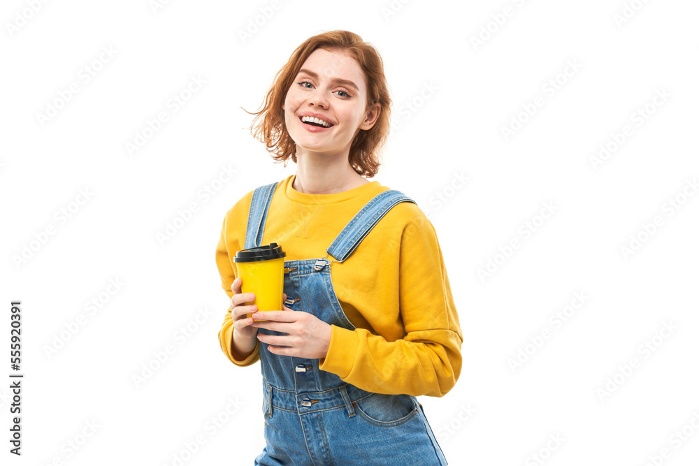 Energetic redhead girl holding and drinking yellow cup of takeaway coffee, smiling and enjoying drink isolated on white background Energetic redhead girl holding and drinking yellow cup of takeaway coffee, smiling and enjoying drink isolated on white background
