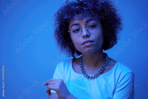 Close-up face portrait of cool kazakh model girl with curls and chain in neon light isolated on studio background