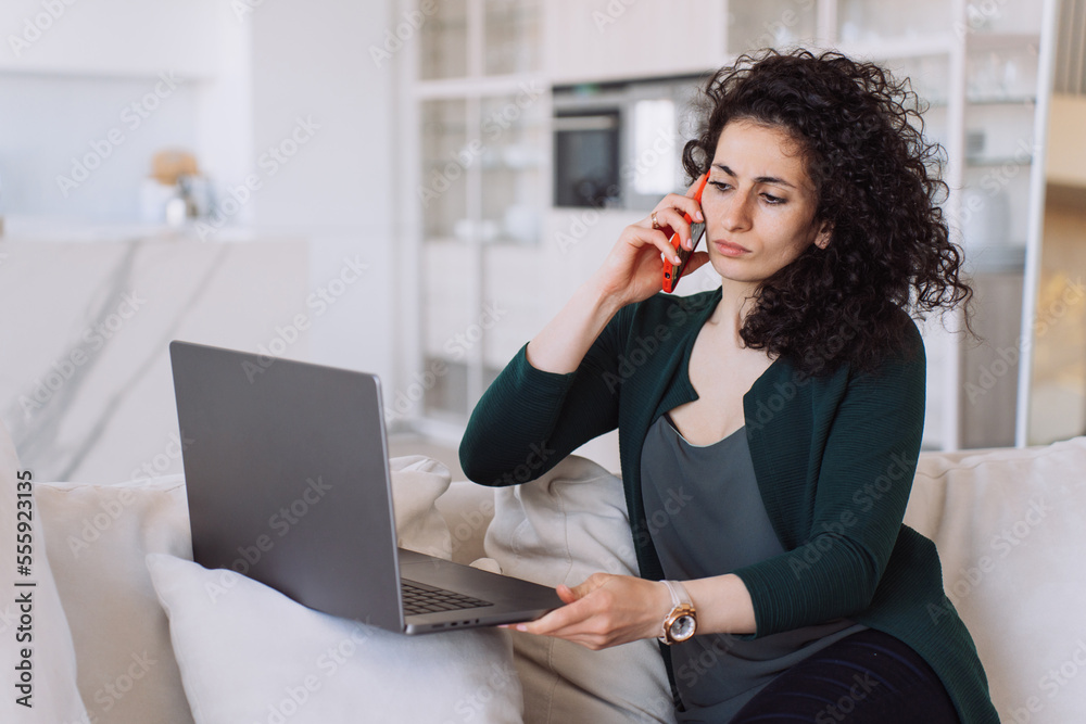 Perplexed curly-haired Spanish woman, talks on phone, sitswith laptop on couch with her eyes open, received unexpected news, upset. Remote working beautiful Spanish businesswoman. Perplexed curly-haired Spanish woman, talks on phone, sitswith laptop on couch with her eyes open, received unexpected news, upset. Remote working beautiful Spanish businesswoman.