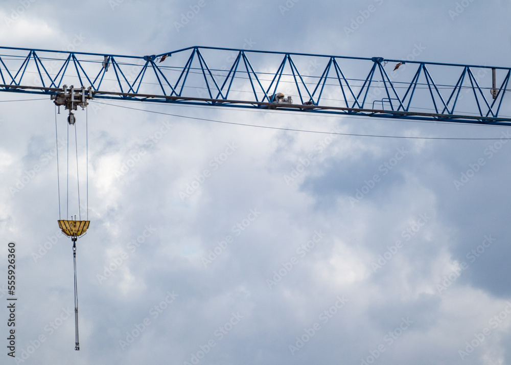 Blue tall crane projecting arm for lifting heavy weights on construction site on cloudy scenic sky background Blue tall crane projecting arm for lifting heavy weights on construction site on cloudy scenic sky background