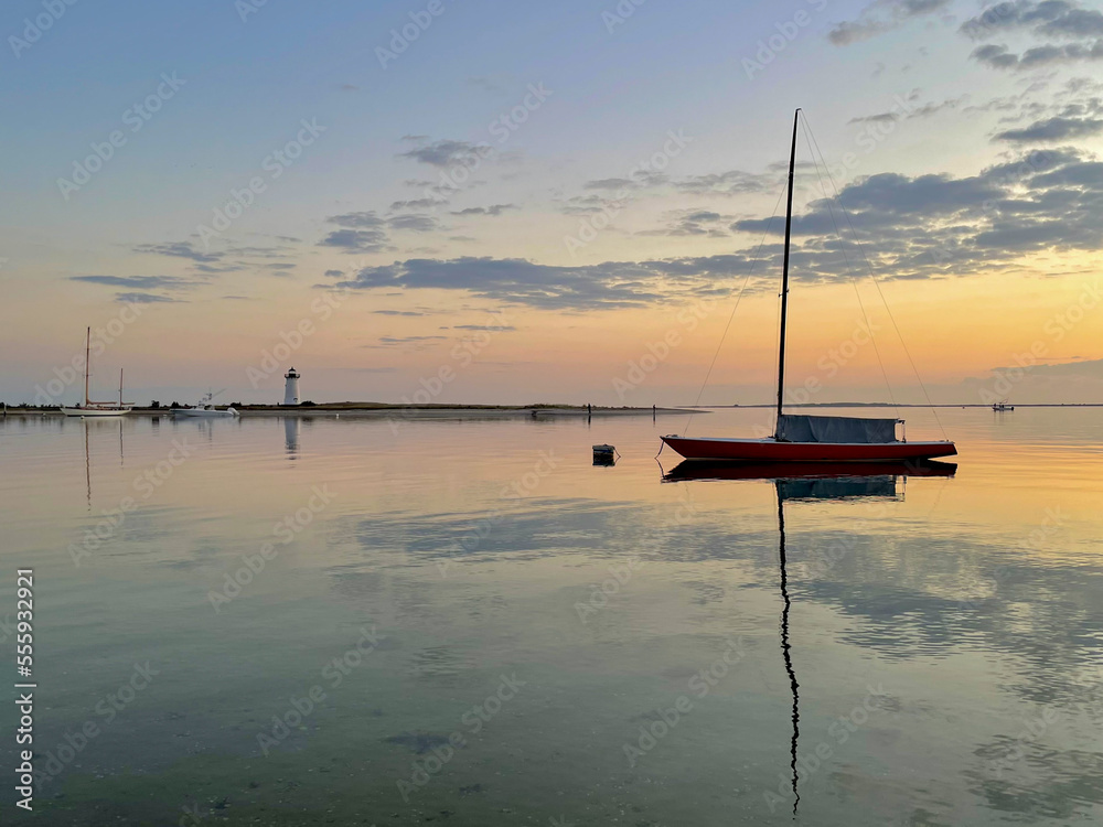 A moored sailboat is reflected in waters of Edgartown Harbor, with the Edgartown lighthouse in the background. A moored sailboat is reflected in waters of Edgartown Harbor, with the Edgartown lighthouse in the background.