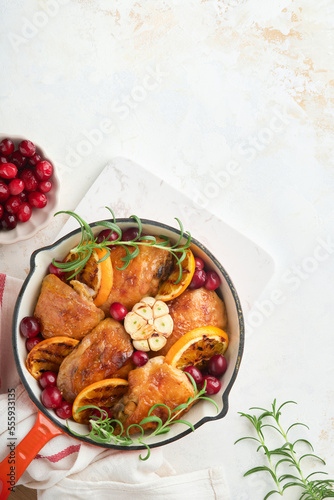 Baked chicken thighs with orange, cranberry and spicy herbs rosemary servered in frying pan on light background. Festive Christmas Dinner Concept menu. Top view. copy space