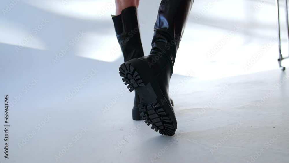 High black leather boots on plain tractor soles on the bare female legs. Model showing the footwear in light studio. High black leather boots on plain tractor soles on the bare female legs. Model showing the footwear in light studio.