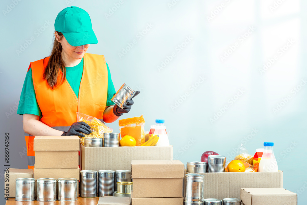 Free Food Distribution. Volunteer sorting food donation box. Young smiling woman wearing uniform cap and t-shirt, orange vest. Girl collects grocery sets, helping in-need people Free Food Distribution. Volunteer sorting food donation box. Young smiling woman wearing uniform cap and t-shirt, orange vest. Girl collects grocery sets, helping in-need people