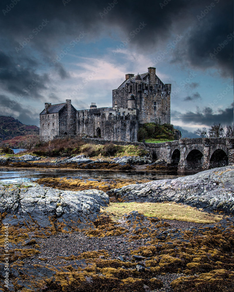 Autumnal portrait view of Eilean Donan Castle in the Scottish Highlands framed by dramatic clouds.