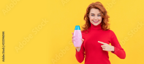 girl curly hair pointing finger on shampoo bottle. hair conditioner advertisement.
