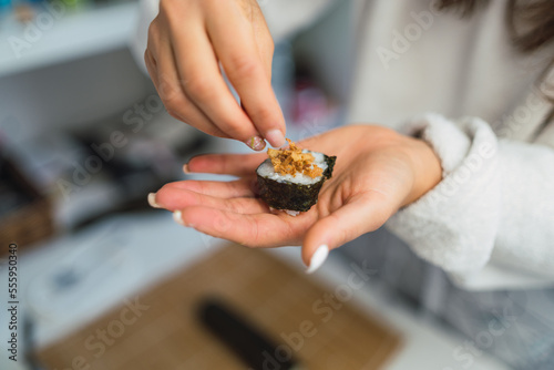 Unrecognizable woman's hands dressing with crispy onion a slice of homemade sushi she has just prepared in her kitchen.