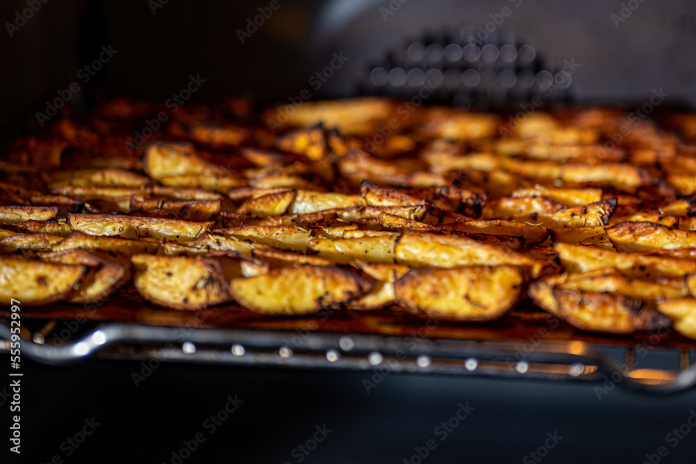 Crispy, golden brown baked potato wedges seasoned with paprika, garlic, salt, pepper, rosemary, basil on tray in the oven photographed from the side.