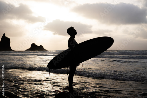 Silhuoette of a surfer at the beach during sunset looking at the sky. photo