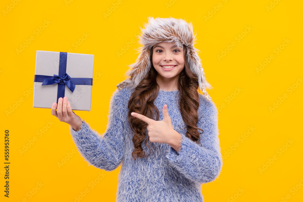 happy child in sweater and earflap hat point finger on present box on yellow background, holiday happy child in sweater and earflap hat point finger on present box on yellow background, holiday