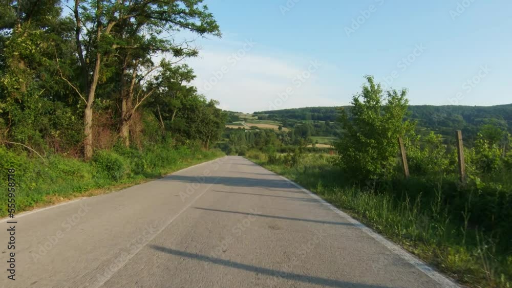 A slow car or motorcycle ride downhill on a winding country road surrounded by vineyards, meadows and trees. Blue sky, summer time. POV shot A slow car or motorcycle ride downhill on a winding country road surrounded by vineyards, meadows and trees. Blue sky, summer time. POV shot