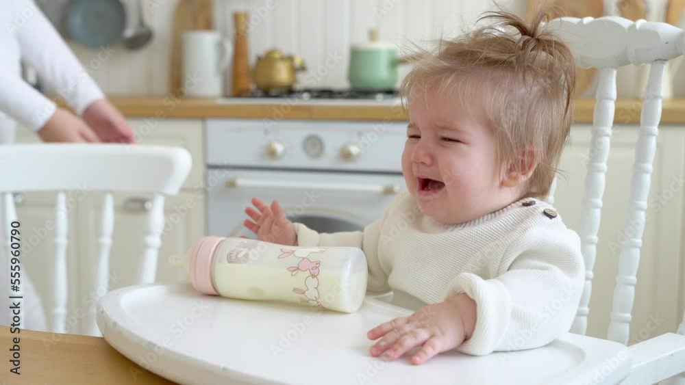 Cute messy baby girl crying while drinks powered milk from a bottle at