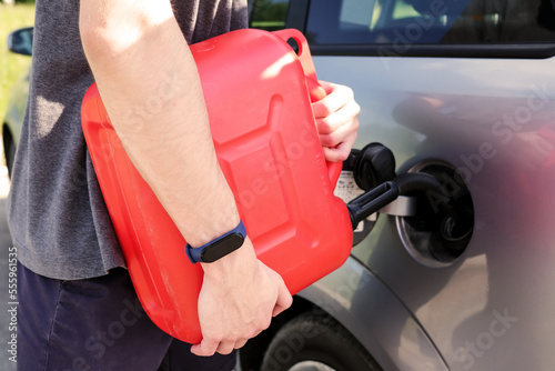 A red canister on the asphalt near the car. The car ran out of gas and stalled. A young man hoping for help on the road from other drivers.