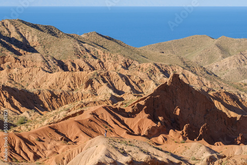 Man climbing hill in the Skazka fairytale canyon. Lake Issyk-Kul in the background. Tosor, Kyrgyzstan photo