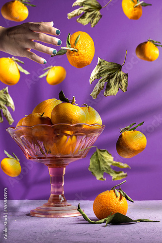 Fototapeta Naklejka Na Ścianę i Meble -  Fresh ripe mandarine with autumn leaves falling in the air and some in stand plate and hand catching a orange fruit with palm shadow Food levitation concept