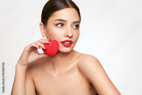 Young beautiful woman with heart-shaped gift. Girl with pure perfect face skin. Cosmetology, beauty and spa. Red nails manicure. Valentine’s Day