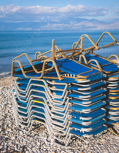 Stack of sunbeds chaise-longues piled up on the beach in the end of touristic season in Greece, Ionian sea islands