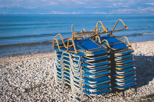 Stack of sunbeds chaise-longues piled up on the beach in the end of touristic season in Greece, Ionian sea islands