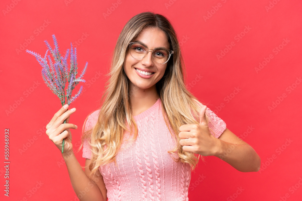 Young pretty Uruguayan woman holding lavender isolated on red background with thumbs up because something good has happened