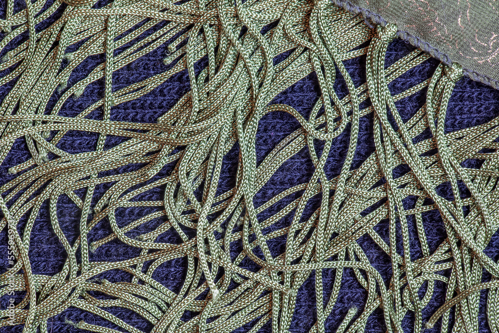 A green silk shawl with a fringe along the edge of the fabric against a dark blue woolen fabric. Abstract background.