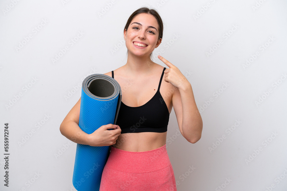 Young sport girl going to yoga classes while holding a mat isolated on white background giving a thumbs up gesture Young sport girl going to yoga classes while holding a mat isolated on white background giving a thumbs up gesture