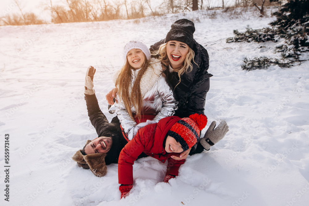 Obraz premium Father, mother and two children daughters are having fun and playing on snowy winter walk in nature. Happy family at sunset. Frost winter season.