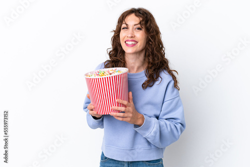 Young woman with curly hair isolated on white background holding a big bucket of popcorns