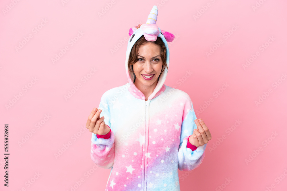 Young caucasian woman with unicorn pajamas isolated on pink background making money gesture Young caucasian woman with unicorn pajamas isolated on pink background making money gesture