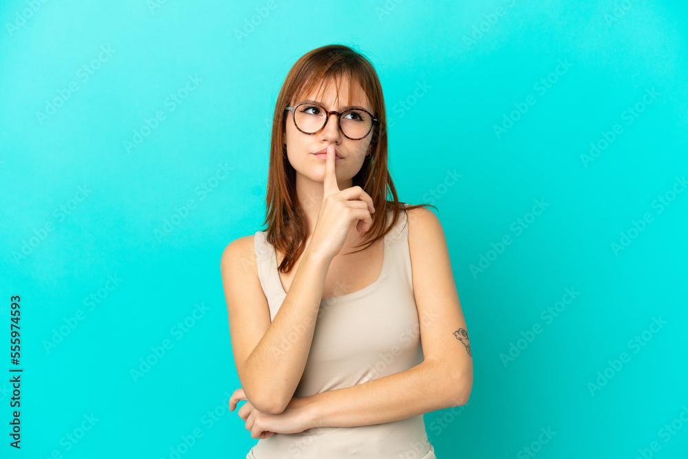 Redhead girl isolated on blue background having doubts while looking up Redhead girl isolated on blue background having doubts while looking up