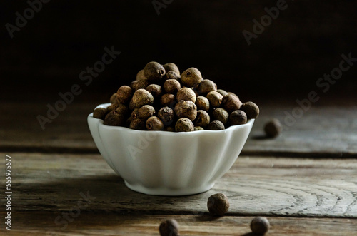 Allspice in a white bowl on a wooden table.ммммммм