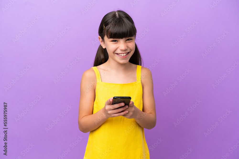 Little caucasian kid isolated on purple background sending a message with the mobile