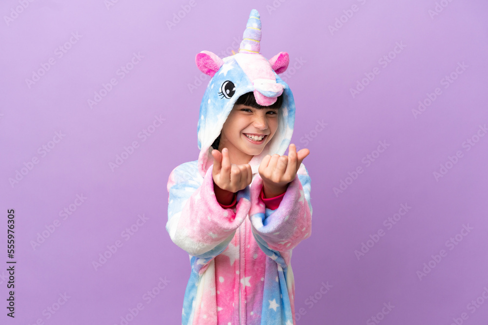 Little kid wearing a unicorn pajama isolated on purple background making money gesture