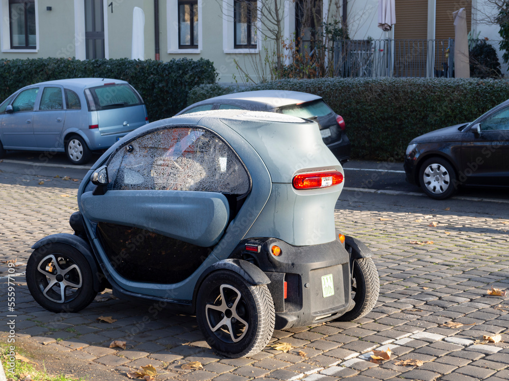 Fototapeta premium Coche pequeño eléctrico aparcado sobre calle de adoquines, recargable y sostenible con energía renovable, 2022 Alemania.