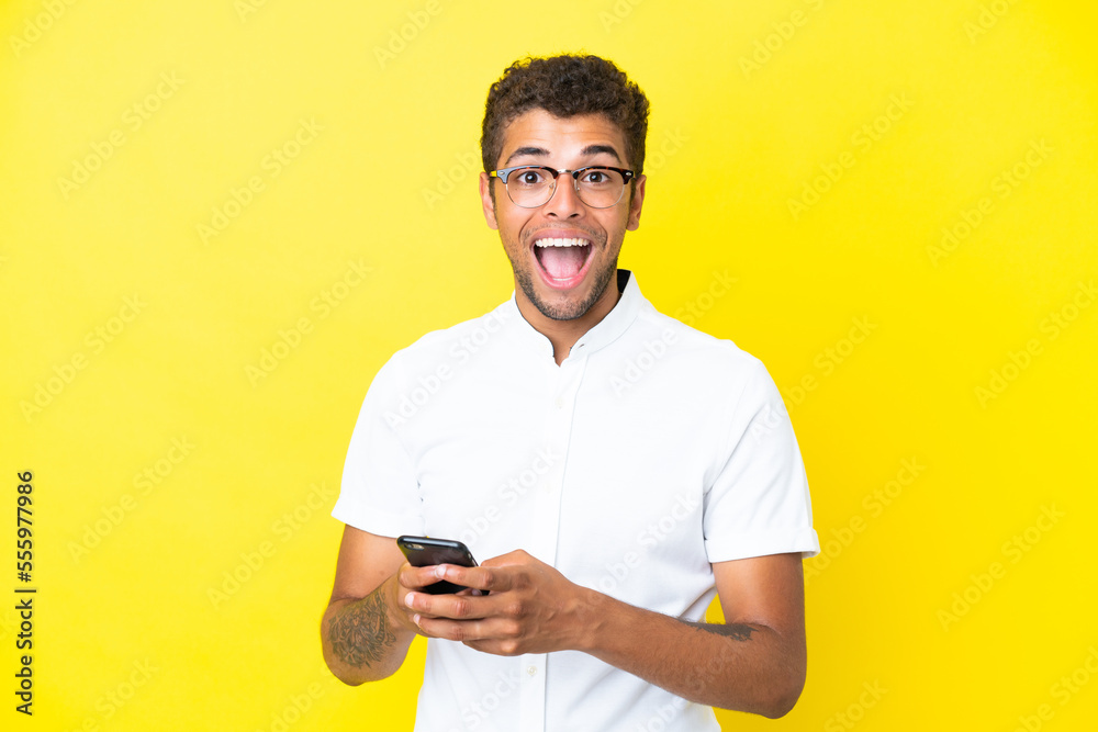 Young handsome Brazilian man isolated on yellow background surprised and sending a message Young handsome Brazilian man isolated on yellow background surprised and sending a message