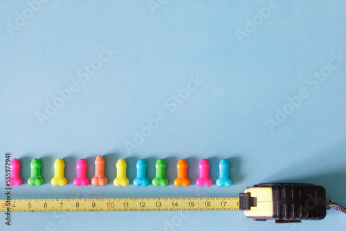 Multi-colored candies that look like small male penises and a yellow measuring tape on a blue background. Concept of comparing sizes and measuring penises. Copy space. Selective focus. photo