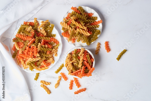 Raw fusilli pasta of different colors on a white marble table