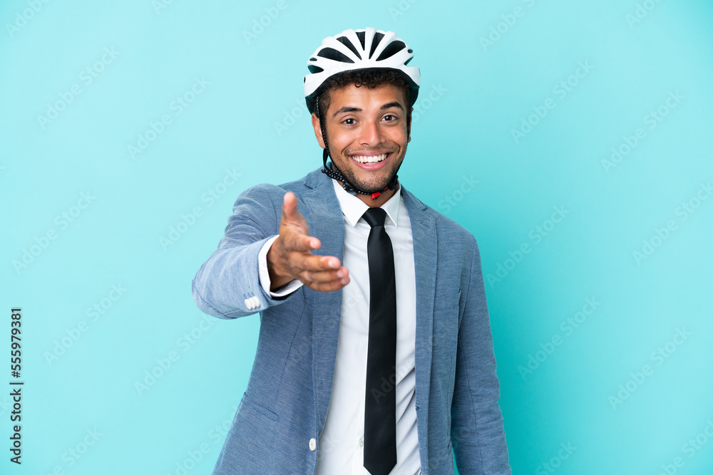 Young business Brazilian man with bike helmet isolated on blue background shaking hands for closing a good deal Young business Brazilian man with bike helmet isolated on blue background shaking hands for closing a good deal
