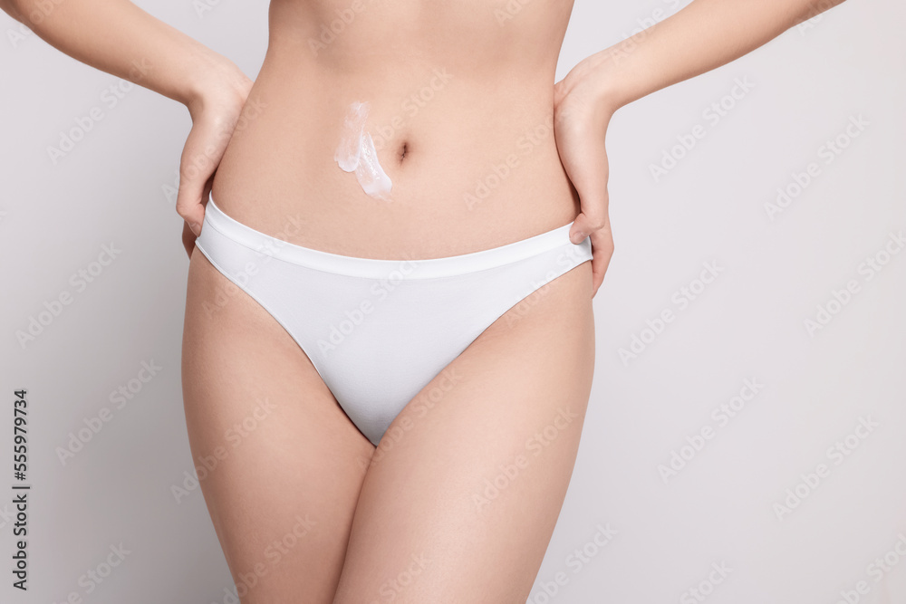 Woman with body cream smear on belly against light grey background, closeup. Space for text