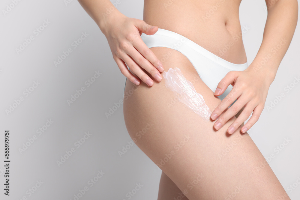 Woman applying body cream onto hip on light grey background, closeup. Space for text