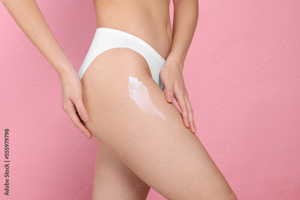 Woman with smear of body cream on leg against pink background, closeup